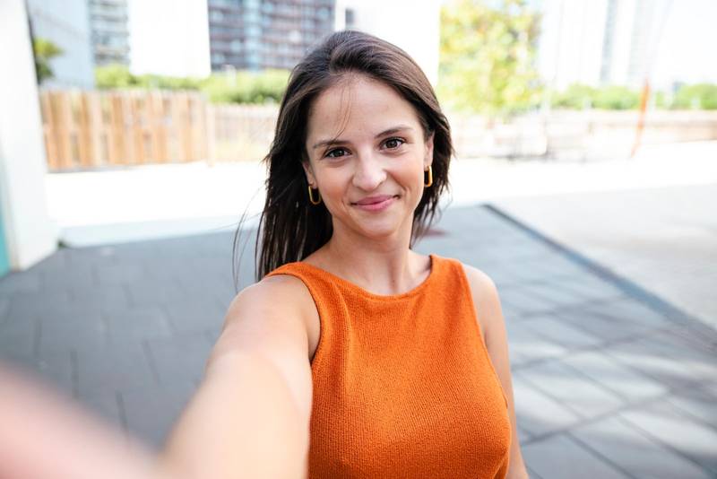 Portrait of a young woman taking a selfie in the city wearing an orange shirt - Wellbeing, healthy lifestyle and happy people concept