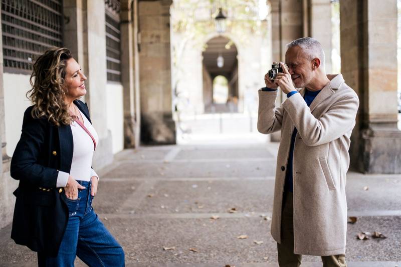 Senior tourist couple taking picture on vintage camera standing in old town. Mid adult man taking photography of her wife posing during romantic trip outdoor.