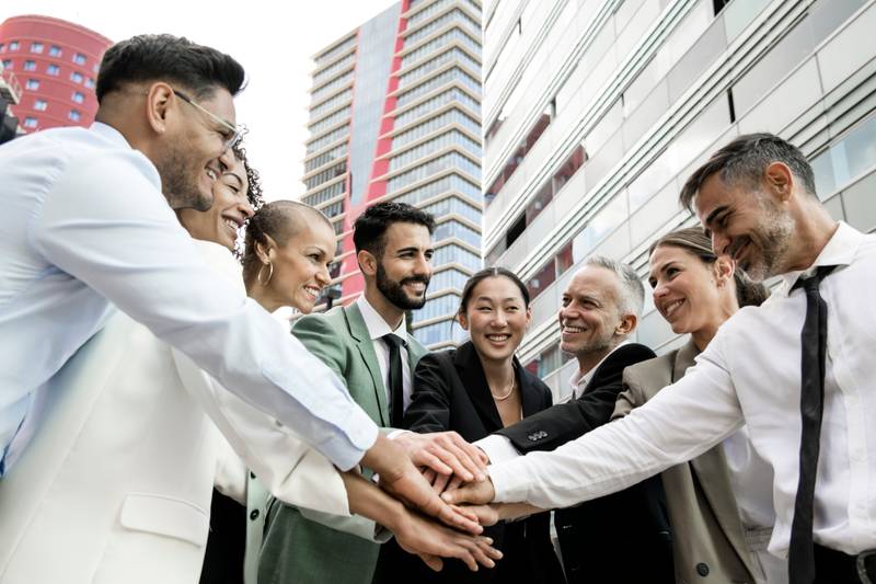 Group of smiling multiethnic businessman and businesswoman holding hands together outside. Multiracial cheerful successful executive team standing in a circle. Teamwork concept.