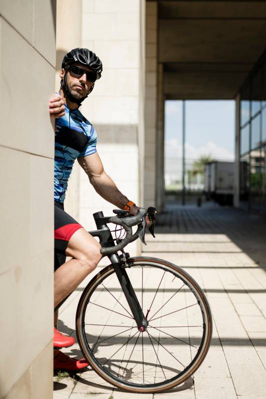 Fit man riding a bike in the city looking at camera. Athletic cyclist male standing on a corner in the street.
