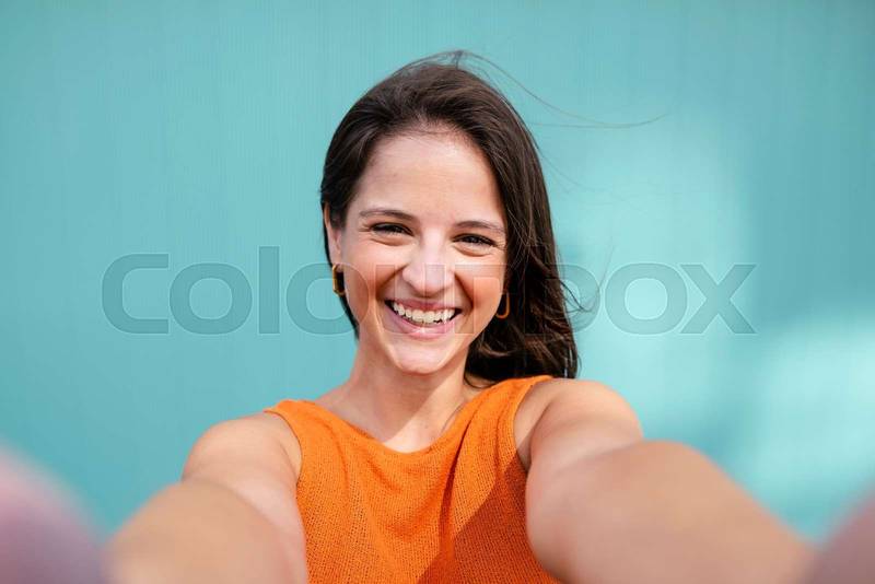 Selfie-portrait of beautiful young woman smiling in turquoise wall - Wellbeing, healthy lifestyle and happy people concept