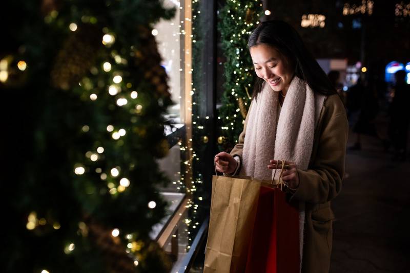 Satisfied young lady looking inside shopping bags in the street. Happy female holding shopping bags in Christmas.