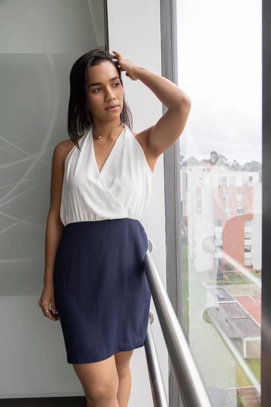 latin woman with short straight hair standing by a window, wearing formal dress
