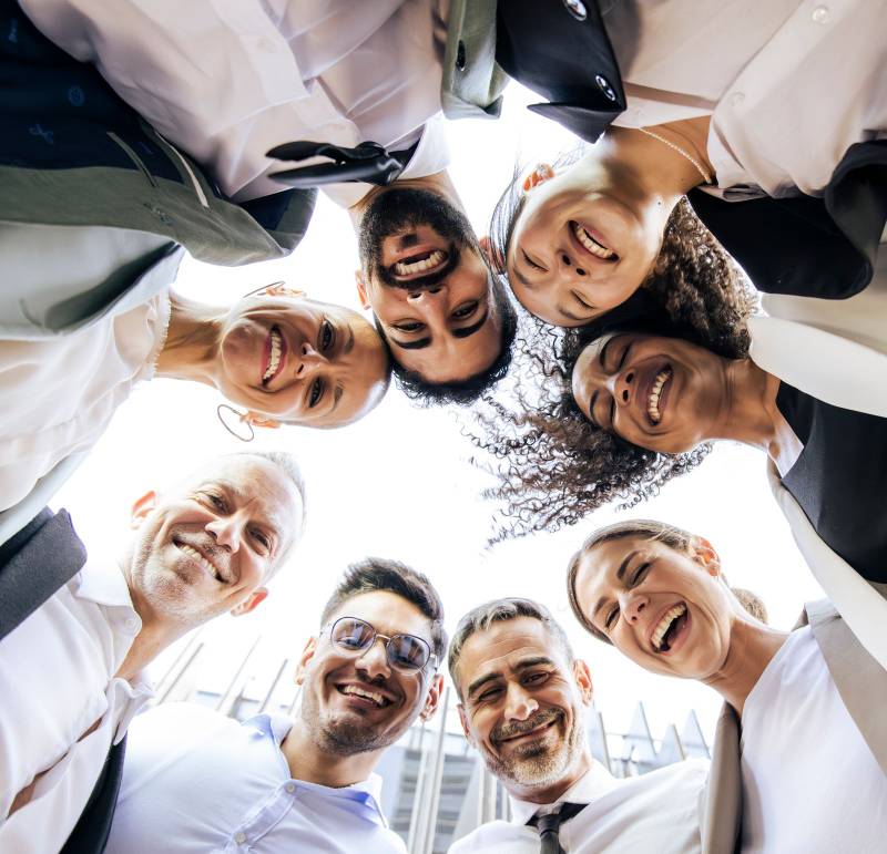 Diverse and cheerful businesspeople standing in a circle in the street. Low angle view of a happy and successful executive team forming a huddle outside. Teamwork concept.