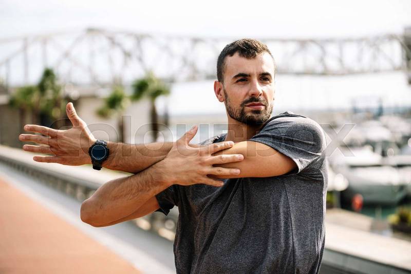 Athlete man stretching before running in the street. Active and sport young male in sportswear warming up for training outside.