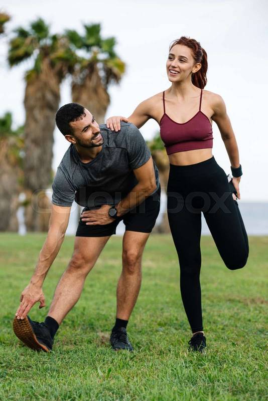 Confident happy and athletic male and female standing in the grass in sportswear training workout outside. Lovely young adult couple warming up in the park after running together. 