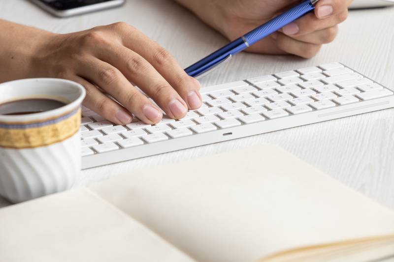 person holding a pen next to a keyboard, winged a notebook with blank sheets, business in the workplace