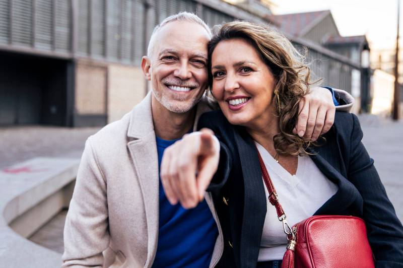 Happy mature couple embracing and looking at each other walking together. Affectionate mid adult man and woman standing and holding arms in the street.