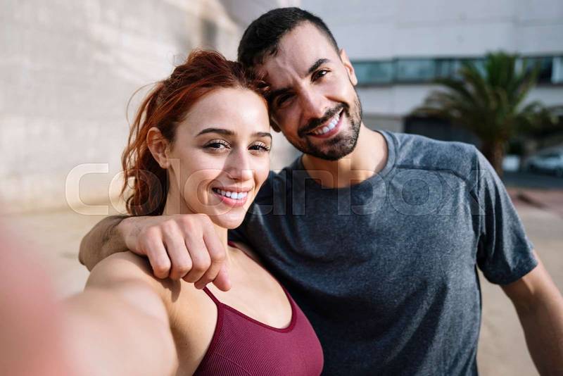 Young fit couple taking selfie smiling after training running outside. Sports lovely joyful active fitness friends standing taking a picture outdoors.