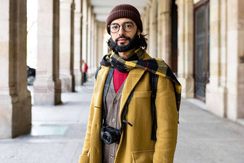 portrait of a fashion tourist man on the street looking at camera. handsome bearded traveler standing in the city. Holidays, travel, fashion concept