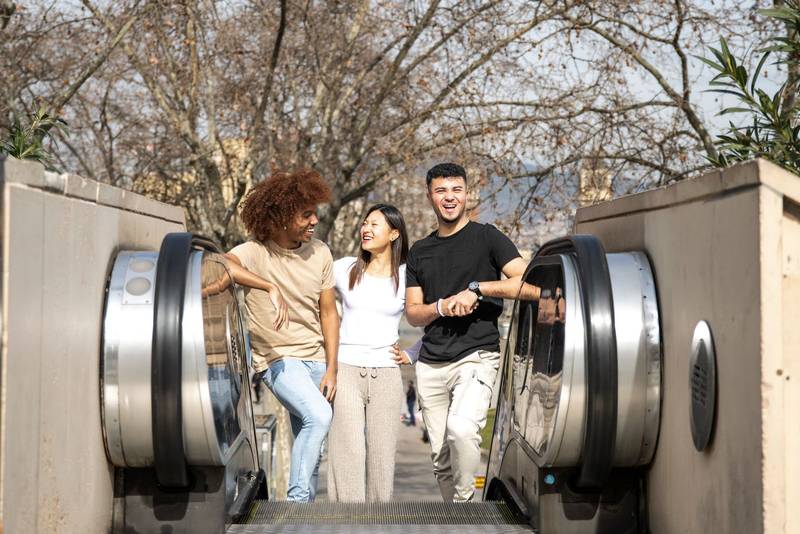 Diverse group of friends going up an outdoor escalator in a park. Three happy young people smiling and looking relaxed climbing up the stairs in the street.