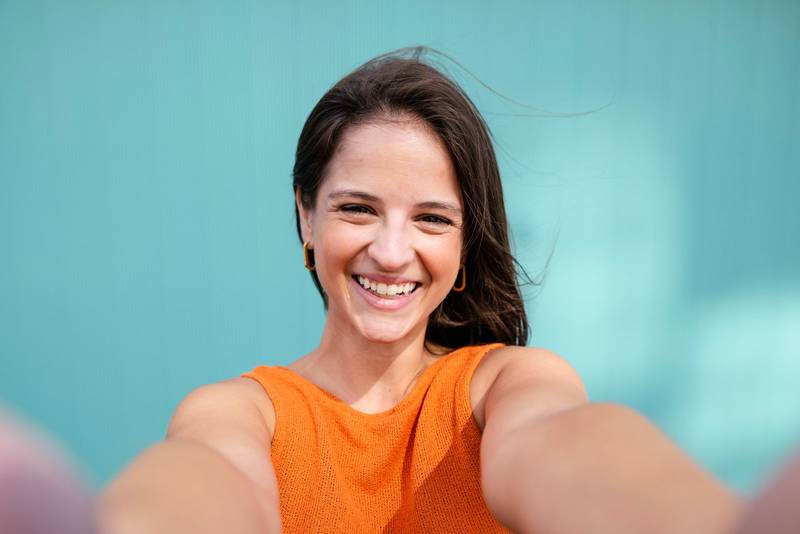 Selfie-portrait of beautiful young woman smiling in turquoise wall - Wellbeing, healthy lifestyle and happy people concept