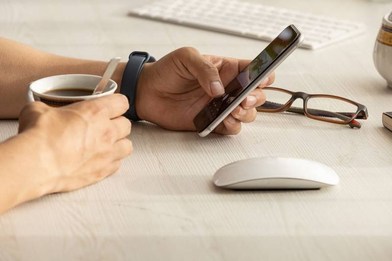 person working at his desk, detail of his hands holding a cell phone
