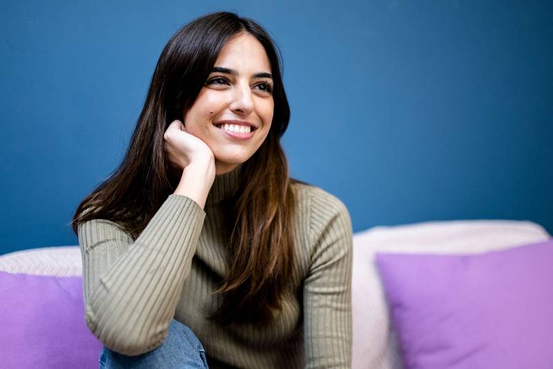 Happy young woman sitting on sofa at home and looking at camera. Portrait of comfortable caucasian woman similing and relaxing on armchair