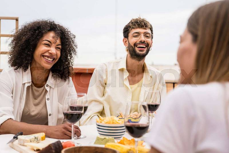 Diverse young people sitting at a terrace table having fun. Cheerful group of friends laughing and chatting while having drinks outdoors.