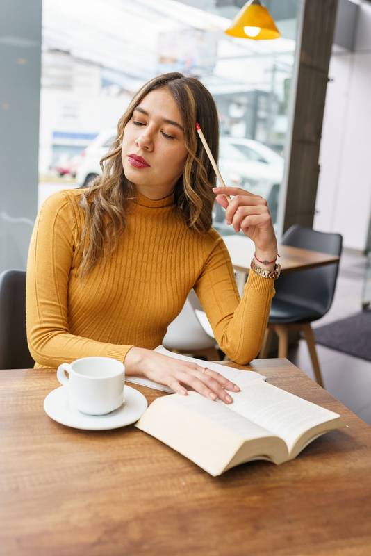 thinking with a pencil on her head a young latin woman with long blonde hair sitting in a cafeteria